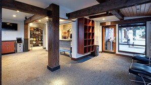 A spacious lobby with a high ceiling, exposed wooden beams, a central column, a reception desk, a glass door leading outside, and a seating area with black chairs. - Snowmass Village 3 Bedroom Deluxe at Crestwood (Snowmass Village)