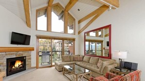 A spacious living room with a fireplace, large windows, a television, and a sofa. - Snowmass Village 3 Bedroom Deluxe at Crestwood (Snowmass Village)