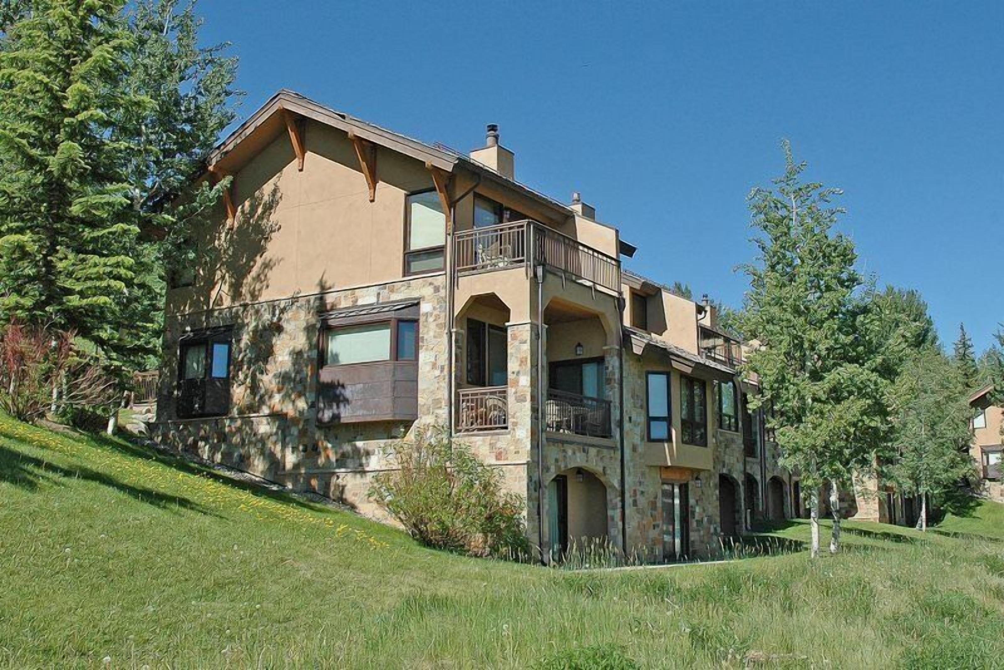 A two-story house with a stone facade, multiple balconies, and a landscaped front yard.