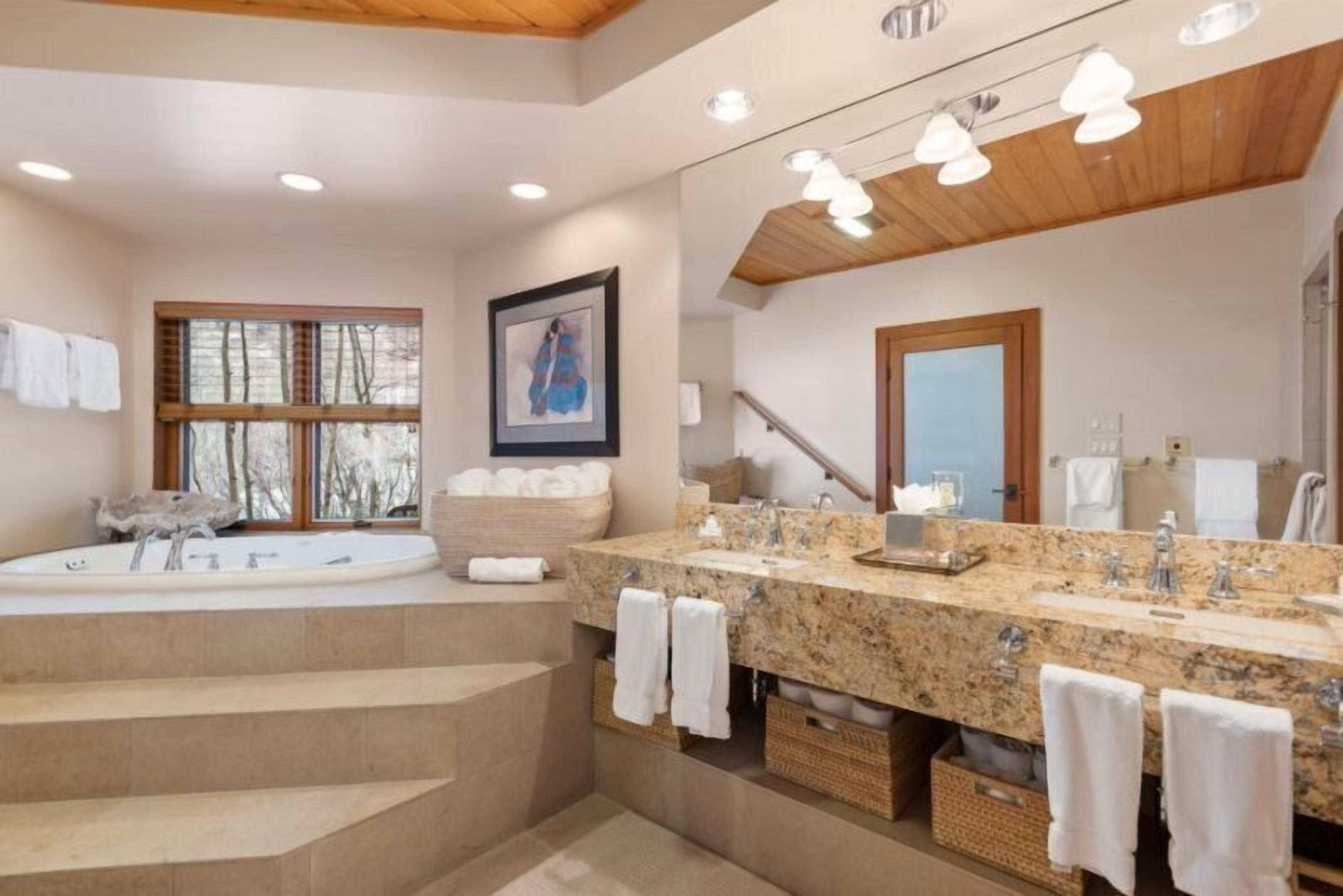A modern bathroom with a large bathtub, a double sink vanity, and a staircase leading to a second floor.