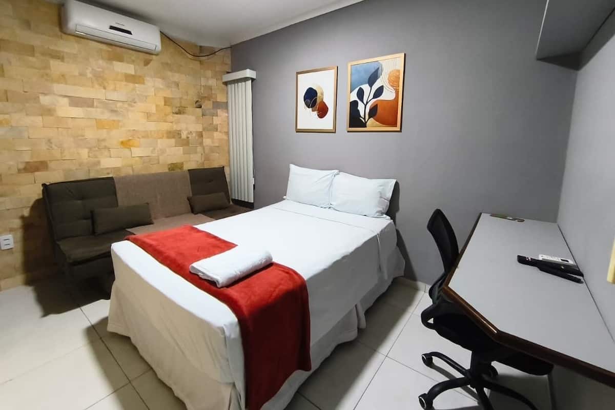 A hotel room with a bed, a desk, a chair, a sofa, and two framed artworks on the wall.