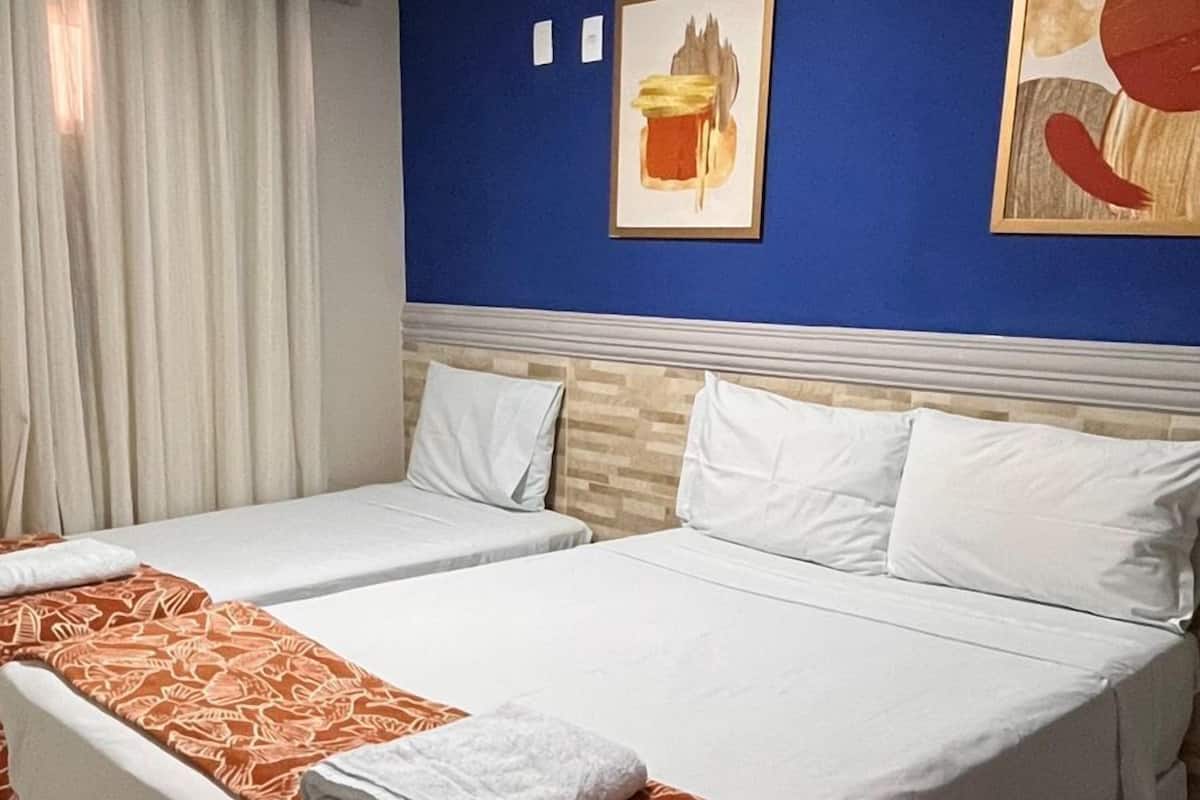 A hotel room with two beds, white bedding, a blue accent wall, and a painting.
