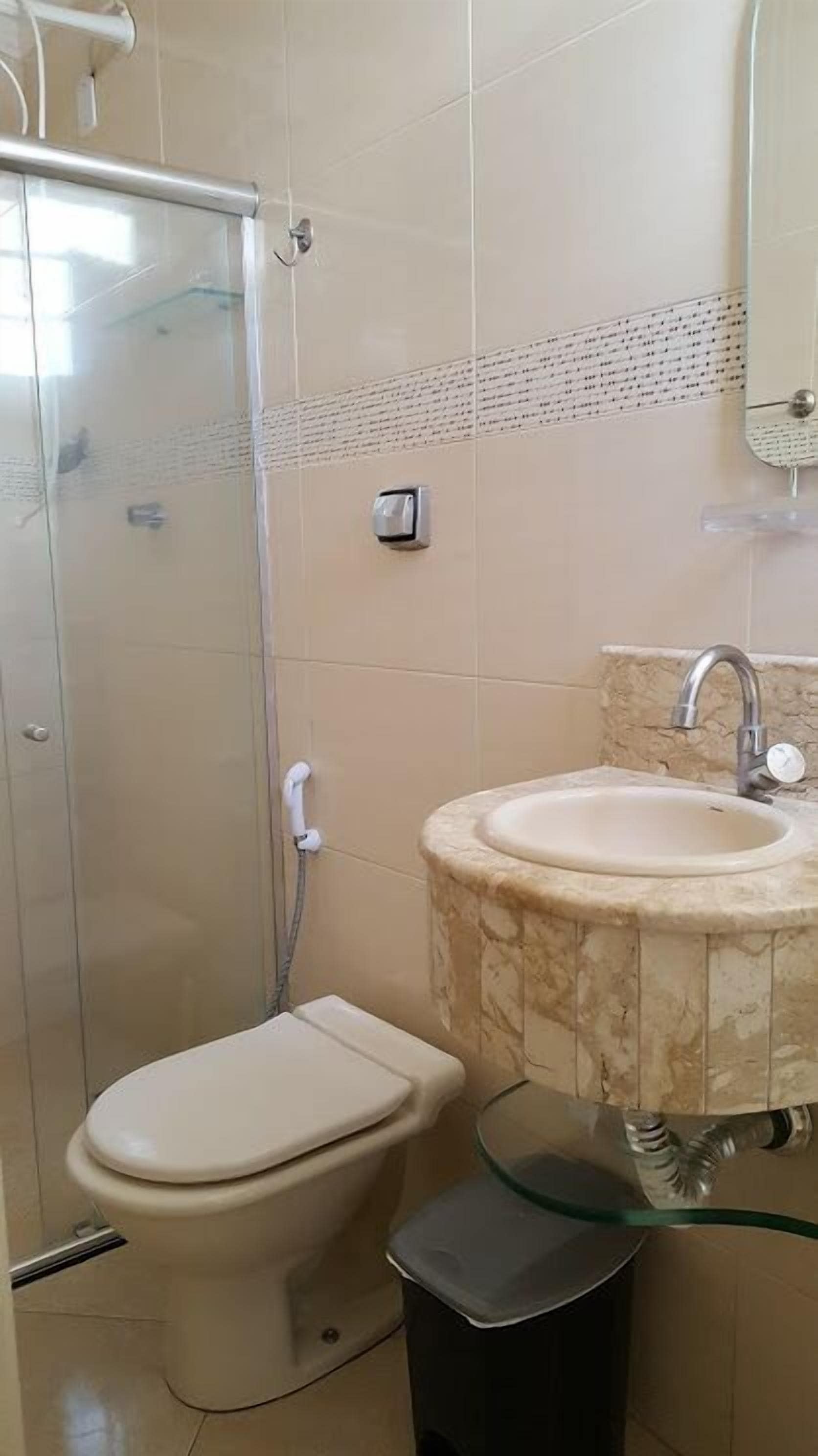 Un baño con inodoro, cabina de ducha de vidrio, lavabo y cubo de basura.