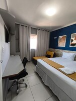 Quarto de hotel com cama, escrivaninha e cadeira.