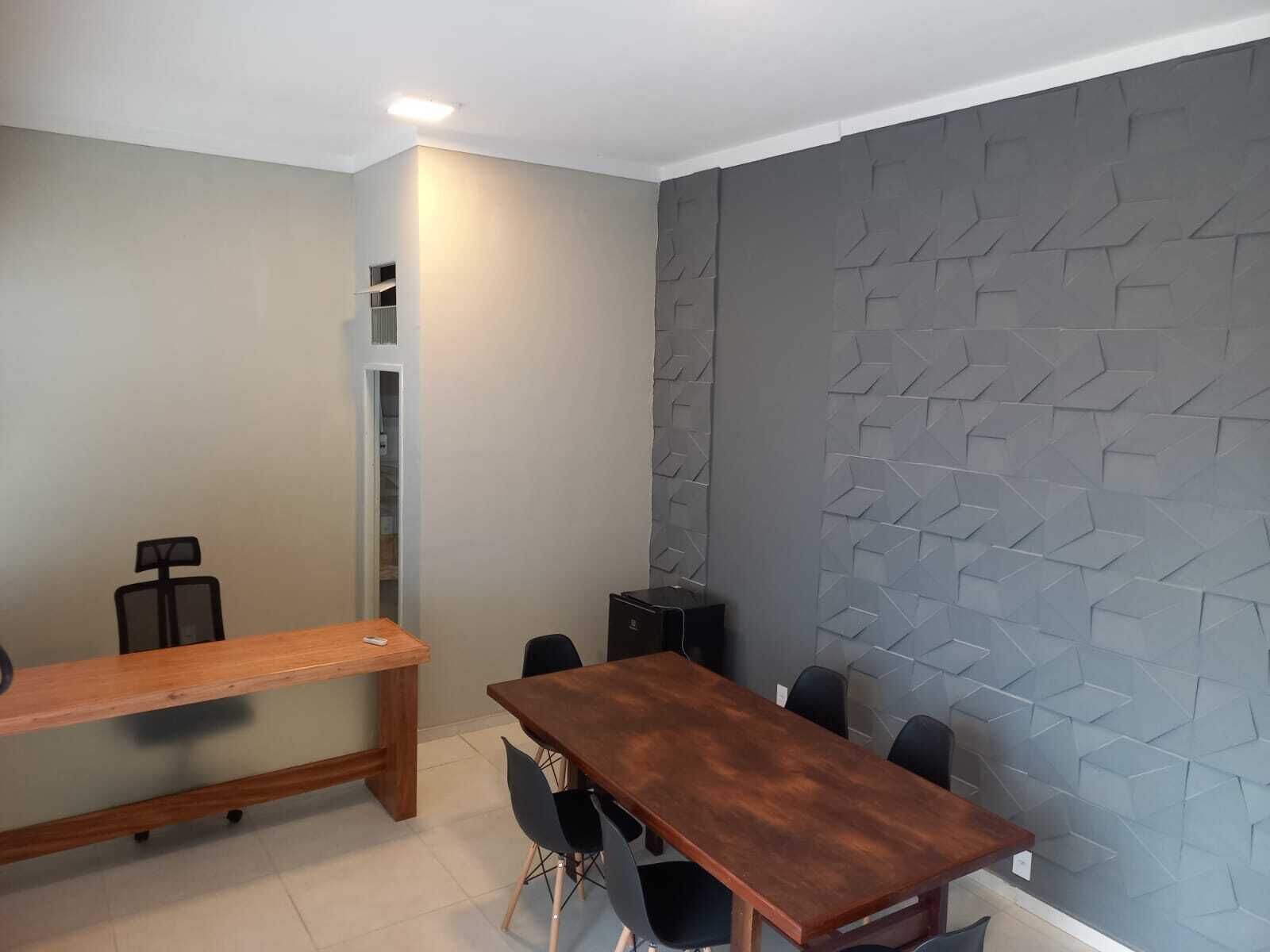 Uma sala de conferência com mesa e cadeiras de madeira, alto-falante embutido e parede cinza texturizada.