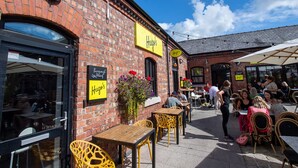 An outdoor seating area with tables and chairs, a brick building with a yellow sign, and a clear blue sky. - Idyllic Bungalow, Ideal Location in West Lancashire (Burscough)