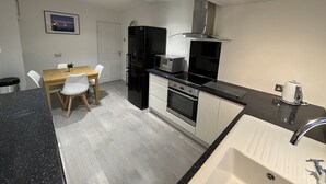A modern kitchen with a black refrigerator, stove, and microwave. There is a dining table with chairs and a small potted plant. - Idyllic Bungalow, Ideal Location in West Lancashire (Burscough)