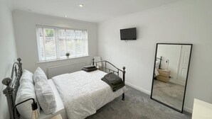 A bedroom with a bed, bedside lamp, window with blinds, and a TV mounted on the wall. - Idyllic Bungalow, Ideal Location in West Lancashire (Burscough)