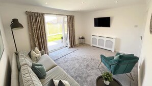 A modern living room with a sofa, a green armchair, a flat-screen TV, and a sliding glass door leading to a balcony. - Idyllic Bungalow, Ideal Location in West Lancashire (Burscough)