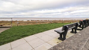 A coastal walkway with benches and a grassy area leading to the sea.