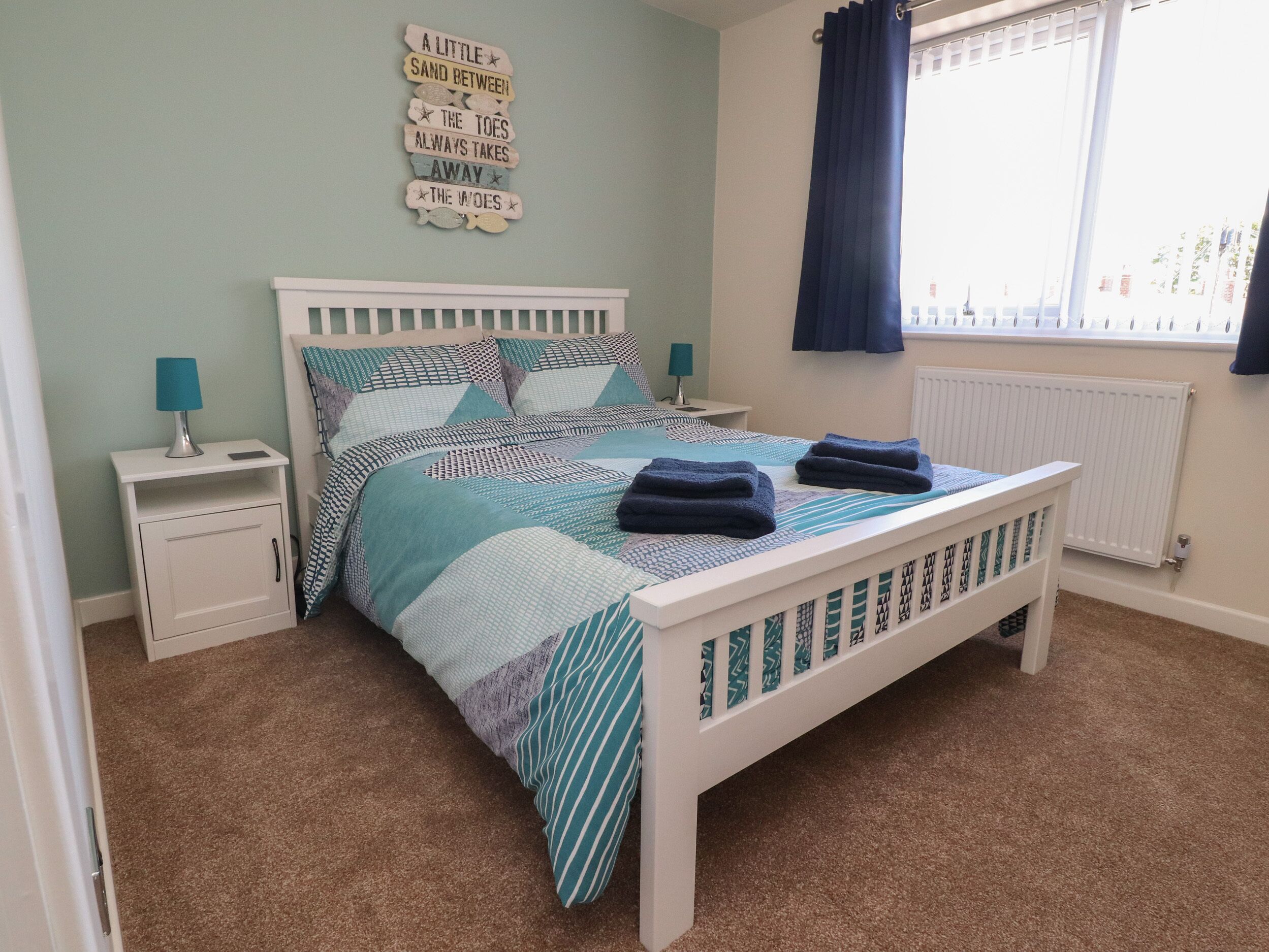 Een slaapkamer met een bed, nachtkastjes, een raam met gordijnen en een wanddecoratie.
