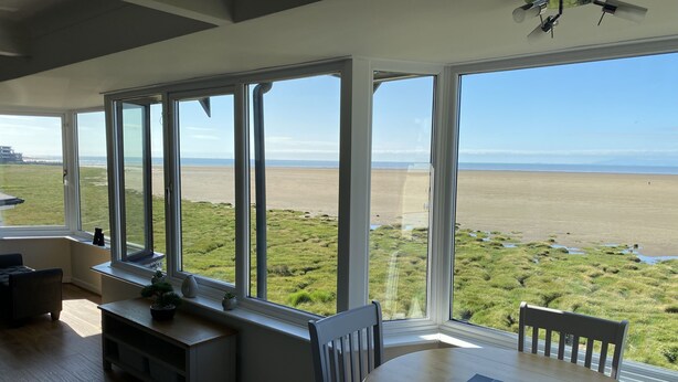 A room with large windows offering a view of a beach and grassy landscape.