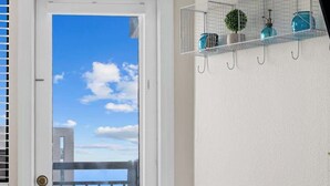 Un balcon avec une porte, une chaise avec un coussin à motifs, un vase avec des fleurs blanches et une table en bois.