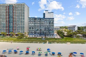 A beachfront hotel with multiple floors, a pool, and beach umbrellas. - Beachside Bliss: Private 1-Bedroom Hideaway (Myrtle Beach)