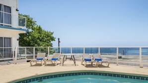 A pool area with lounge chairs and a view of the sea.