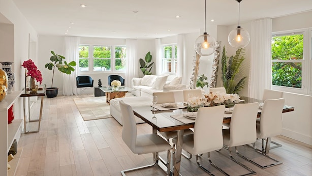 A spacious dining area with a wooden table, white chairs, and hanging pendant lights.
