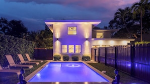 A modern house with a swimming pool, a covered patio, and a fenced backyard.
