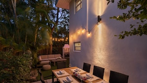 An outdoor dining area with a wooden table set for six, surrounded by chairs.