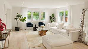 A modern living room with a white sofa, a glass coffee table, and a large potted plant.