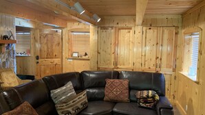 A cozy room with a leather sectional sofa, wooden walls, and built-in cabinets. - Mountain Cabin: 2 bed/2 bath, Fire pit, Close to Yellowstone and a moose family! (Island Park)