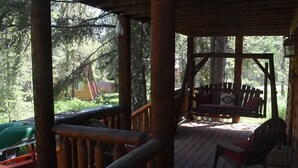 A wooden deck with a bench and chairs, surrounded by trees. - Mountain Cabin: 2 bed/2 bath, Fire pit, Close to Yellowstone and a moose family! (Island Park)