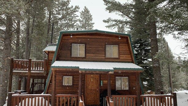 A wooden cabin with a porch, surrounded by snow-covered trees. - Mountain Cabin: 2 bed/2 bath, Fire pit, Close to Yellowstone and a moose family! (Island Park)