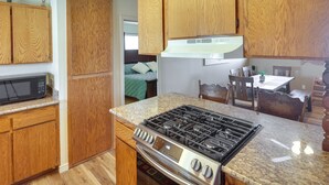 A compact kitchen with wooden cabinets, a built-in microwave, a gas stove, and a dining area with a table and chairs. - Dog-Friendly Bullhead City Home - Walk to River! (Bullhead City)