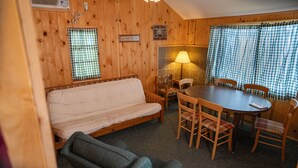 A cozy room with a wooden interior, a sofa, a dining table with chairs, and a lamp. - Webb Lake, Hackensack, Northern MN - 3 Bedroom, Sleeps 6 - Cabin #1 Blue Water (Hackensack)