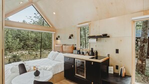Une chambre à coucher de taille modeste, comprenant un lit, une table de chevet et une fenêtre donnant sur une forêt.