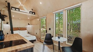A modern bedroom with a large bed, a wooden desk, and a dining area with two chairs. - Lumen Nature Retreat | Cabin HYGGE-ASTRID (North Woodstock)