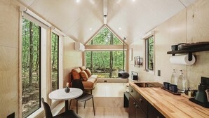 Un interior compacto y moderno con cocina, comedor y una zona de estar acogedora con vistas al bosque.