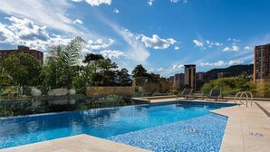 A swimming pool with clear blue water, surrounded by a tiled deck and lounge chairs. - Stunning views from 25th-floor condo! El Poblado! (Medellín)