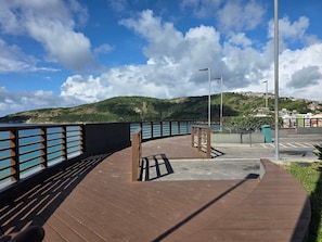A wooden deck with a metal railing overlooking a body of water and a hilly landscape. - Aconchegante Apto na Prainha Arraial (Arraial do Cabo)