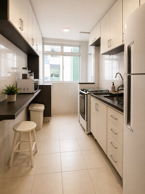 Una cocina moderna con armarios blancos, estufa, pileta y ventana.