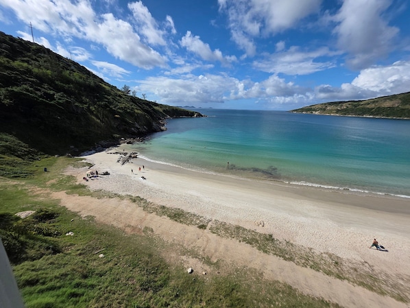 A beach with clear water, a sandy shore, and a hilly landscape in the background. - Aconchegante Apto na Prainha Arraial (Arraial do Cabo)