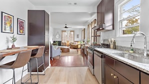 A modern kitchen with a large island, a dining area with a wooden table and chairs, and a living room with a sofa and a coffee table.