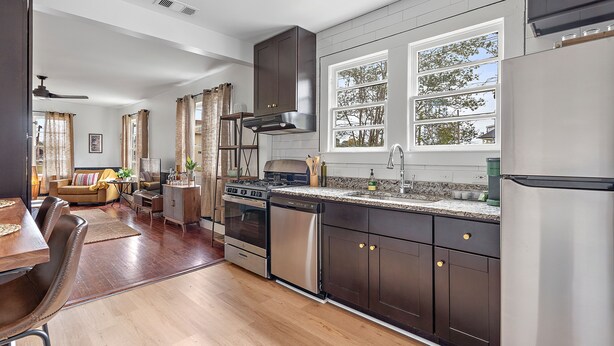 A modern kitchen with dark cabinets, stainless steel appliances, and large windows.