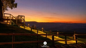 A wooden observation deck with a chain-link fence, overlooking a hilly landscape during twilight.