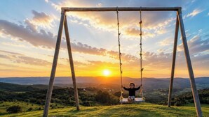 A swing set in a grassy field with a sunset in the background.