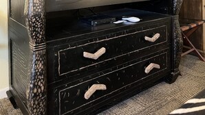 Un meuble de rangement en bois foncé, doté d’un téléviseur à écran plat, de trois tiroirs et d’une petite étagère.