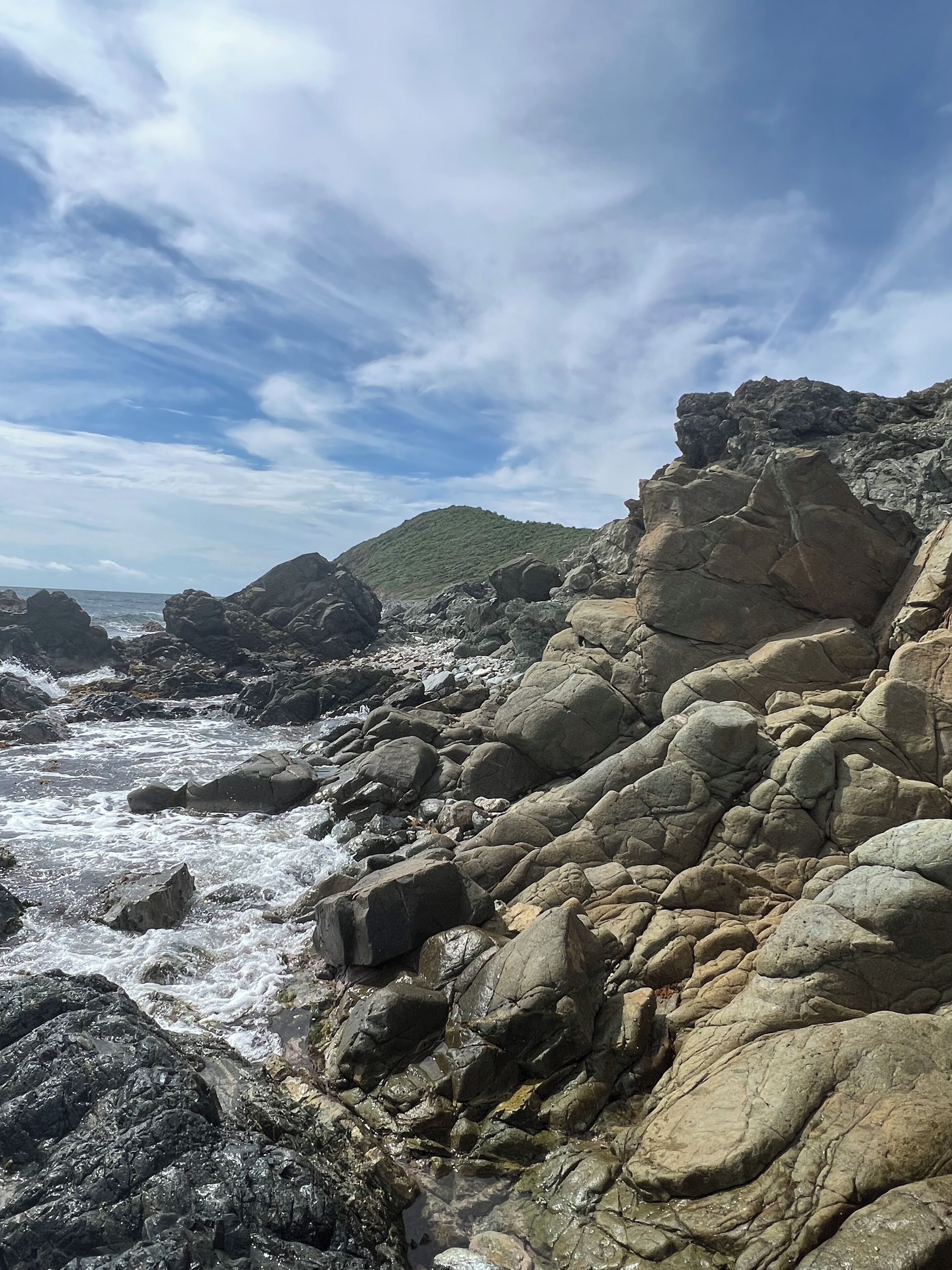A rocky coastal landscape with large boulders and a view of the sea.