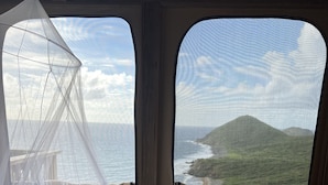 Una cama con colcha de motivos marinos, mosquitera y almohadas, con vistas a un paisaje costero.