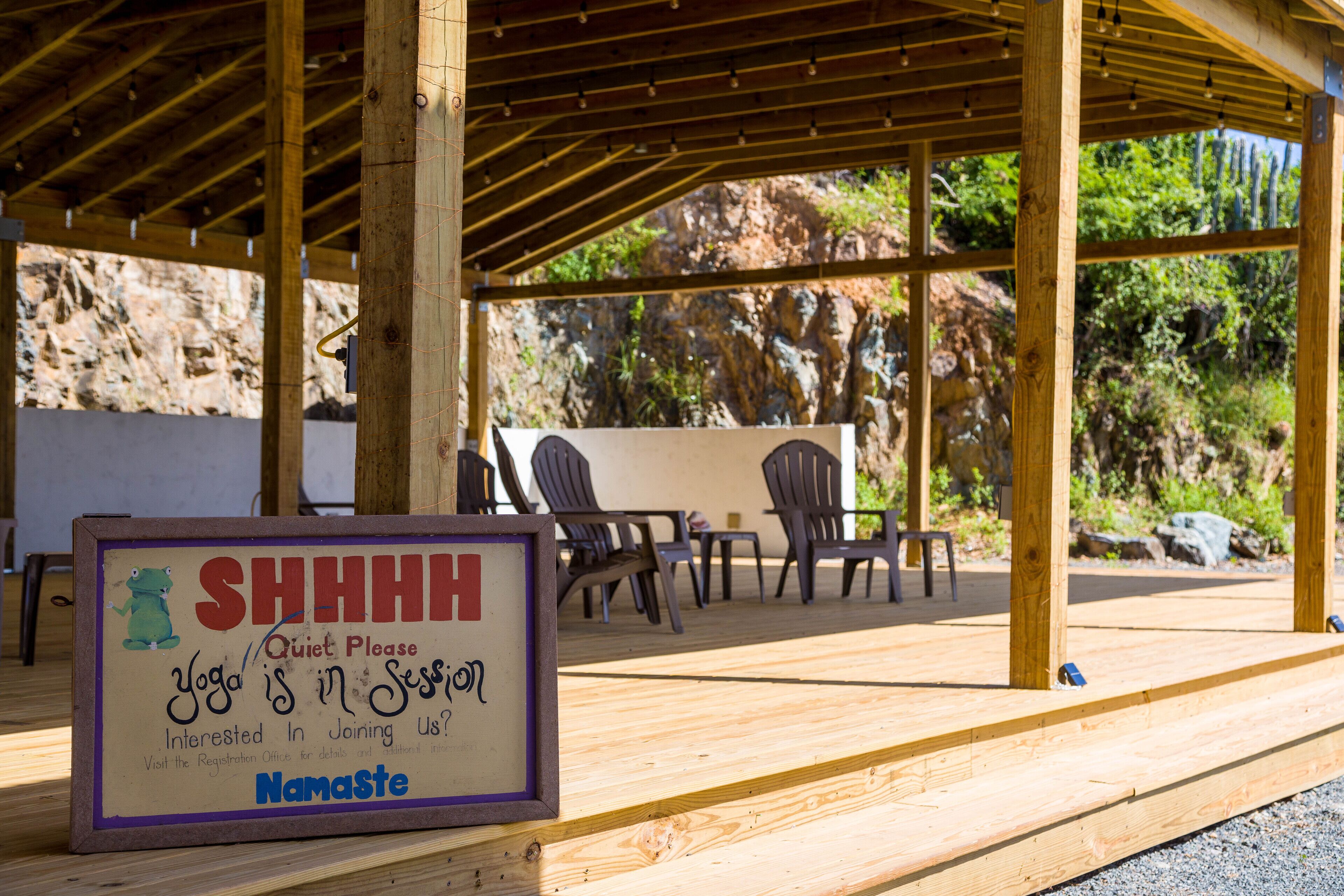 Une terrasse en bois avec une pancarte indiquant « Silence, cours de yoga en cours » et le logo de Namaste.