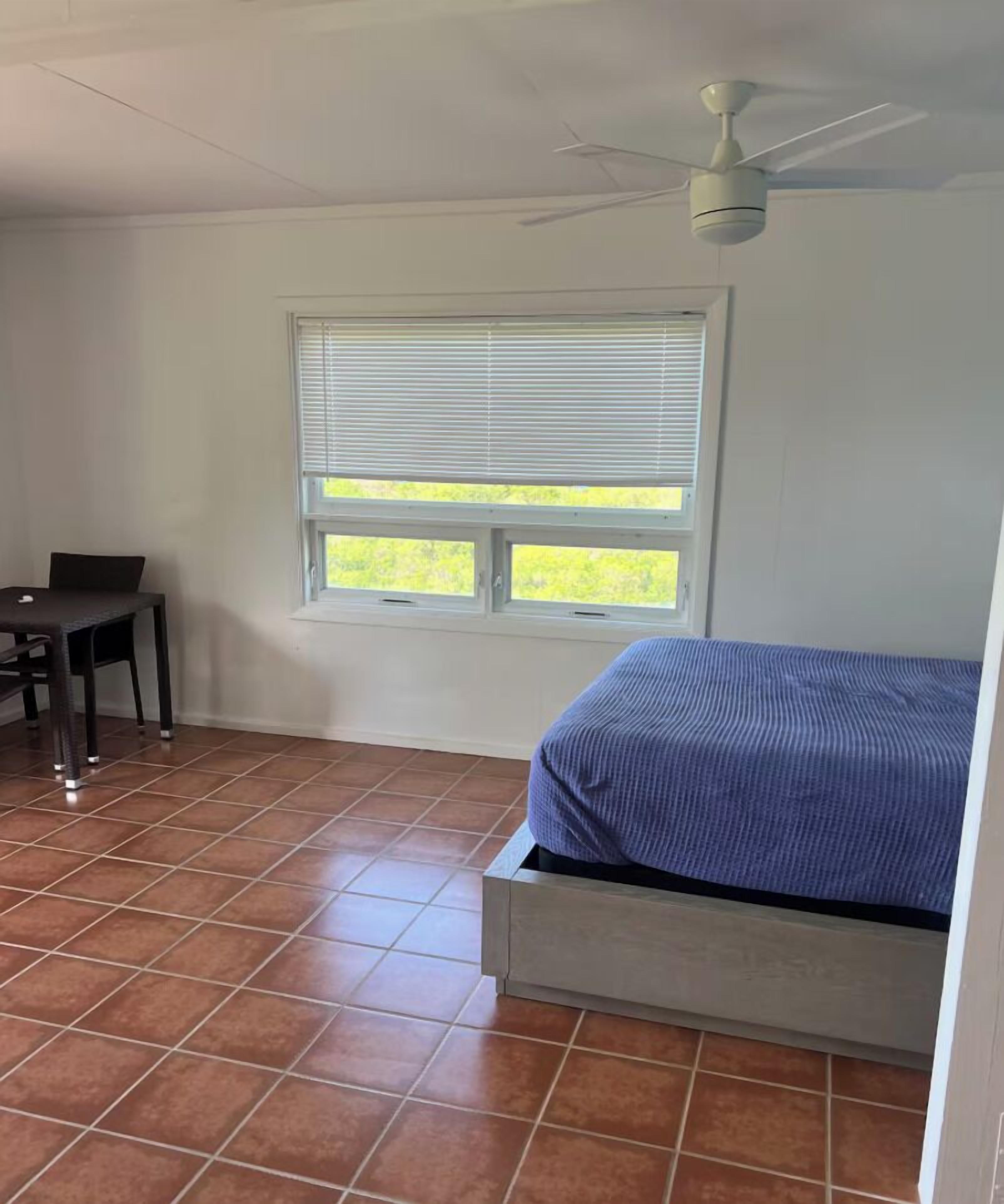 Quarto com cama, escrivaninha, cadeira, janela com persianas e ventilador de teto.