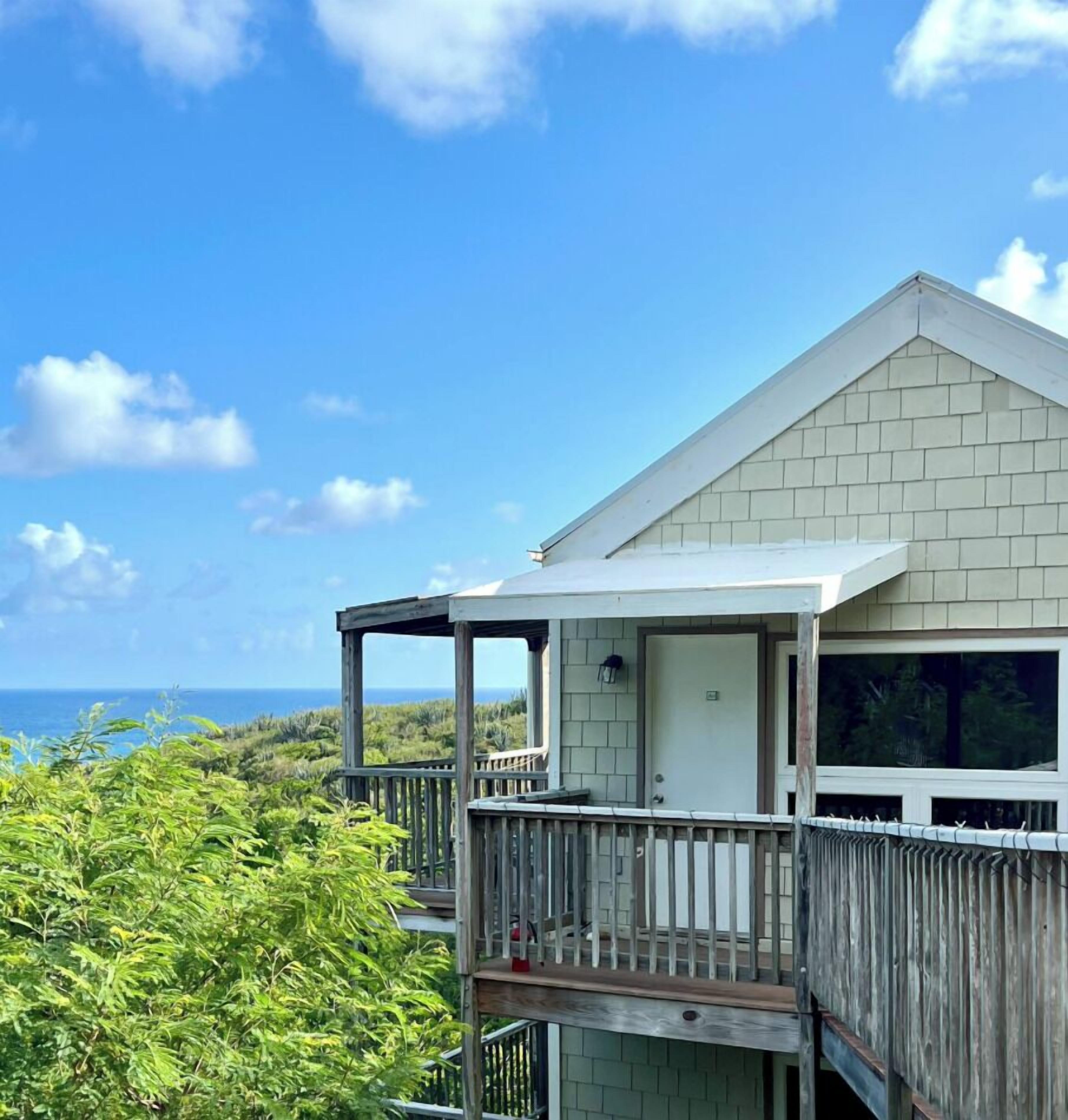 Een huis aan de kust met een balkon dat uitkijkt over de oceaan, een deur en een klein portaal.
