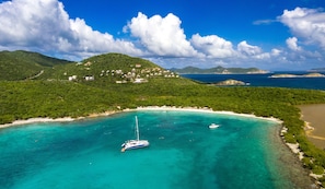 A coastal area with a small boat anchored near a beach, surrounded by lush green hills and clear turquoise waters. - Concordia Eco-Resort (St. John)