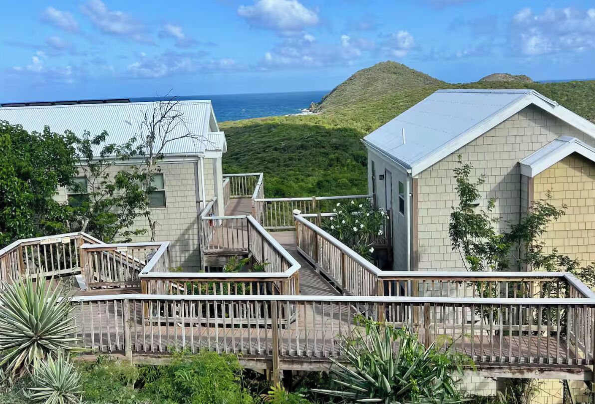 Ein Resort mit Holzterrasse, Blick auf das Meer und einer hügeligen Landschaft.