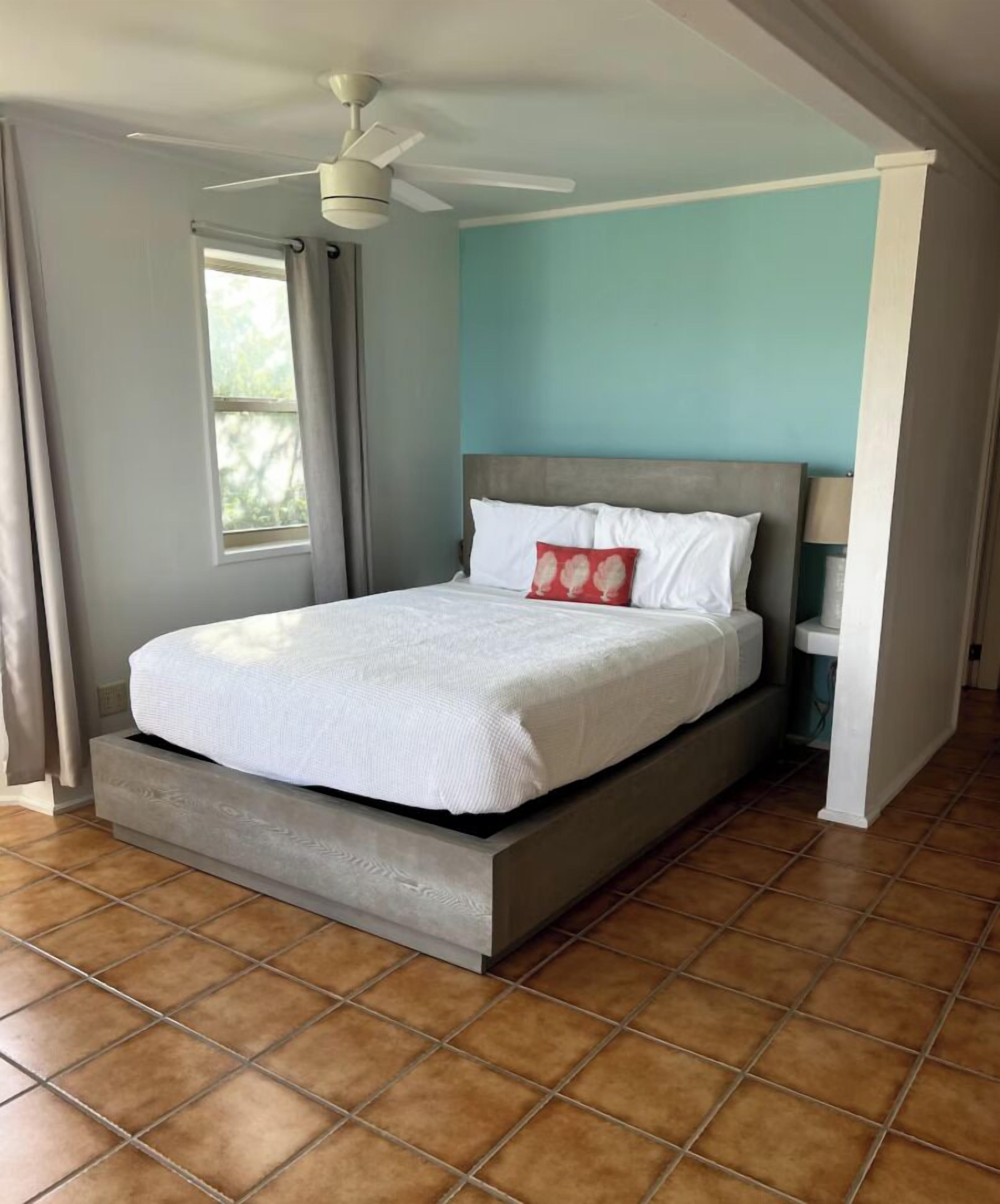 A bedroom with a bed, a ceiling fan, a window with curtains, and a tiled floor.