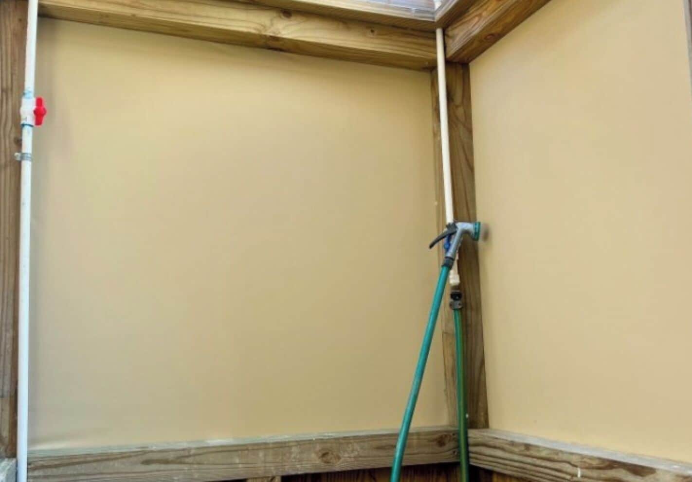 Un coin de pièce avec un plafond en bois et un tuyau vert fixé à un robinet mural.
