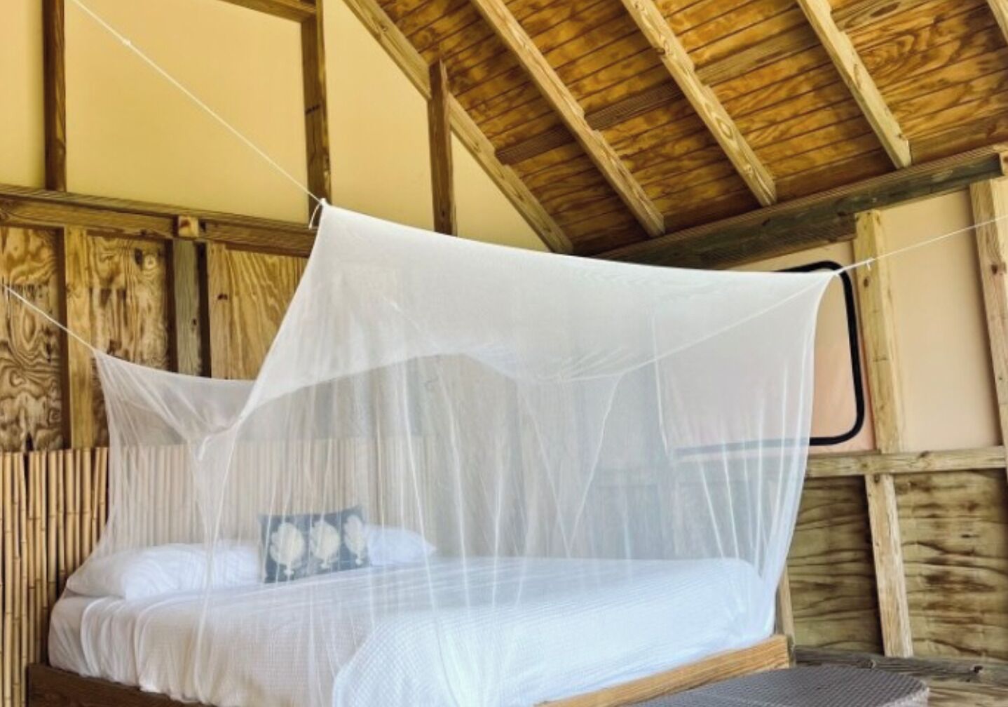A bed with a white mattress and a mosquito net. The room has wooden walls and a sloped ceiling.